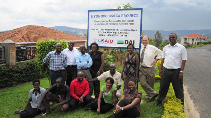 A safari vehicle driving through Akagera National Park, with zebras grazing in the background.