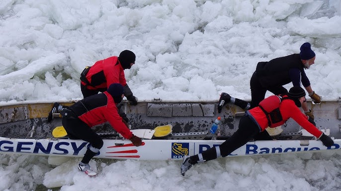 A group of people in brightly colored waterproof gear battling ice floes in the St. Lawrence River, with Quebec City in the background.