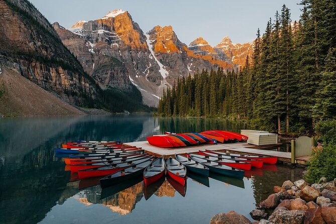 Golden larches reflected in the turquoise waters of Lake Louise, Banff National Park, surrounded by snow-dusted peaks of the Canadian Rockies.