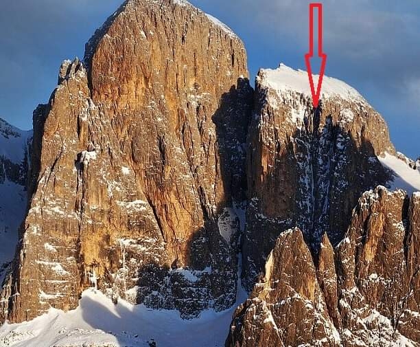 A hiker ascending the Via Ferrata Ivano Dibona with snow-capped peaks in the background, showcasing the scale and beauty of the landscape.