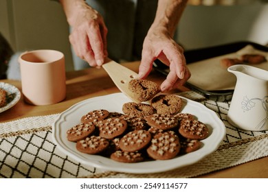 Hands arranging freshly baked chocolate pastries on a wooden surface, illustrating the art of homemade baking