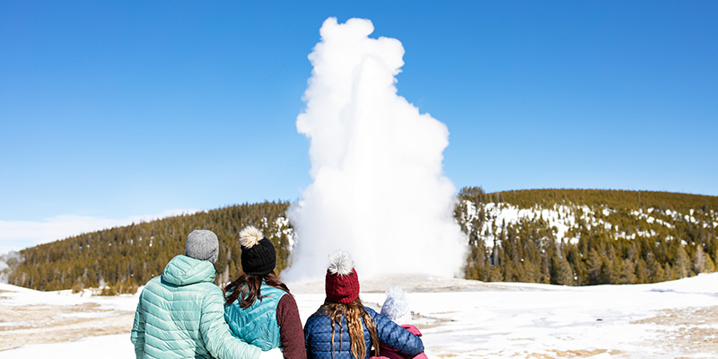 A cyclist rides a fat bike through a snow-covered trail in Yellowstone National Park, with steaming geysers in the background. This illustrates the adventurous spirit and the unique natural wonders available for capture with a drone.