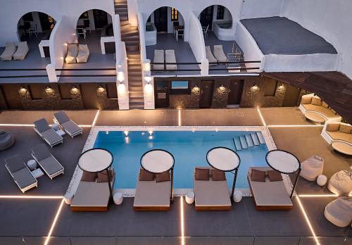 A modern, minimalist hotel room with a private balcony offering stunning caldera views. The room features whitewashed walls, natural wood accents, and simple, elegant furniture.
