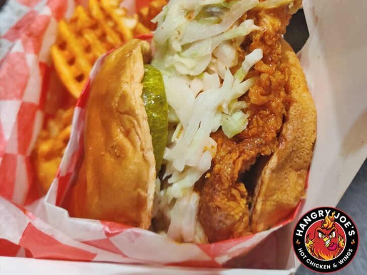 A wide shot of a colorful mural in The Gulch, with Sarah posing in front of it at sunset, throwing up a peace sign, while a small dog humorously pees on the bottom of the mural