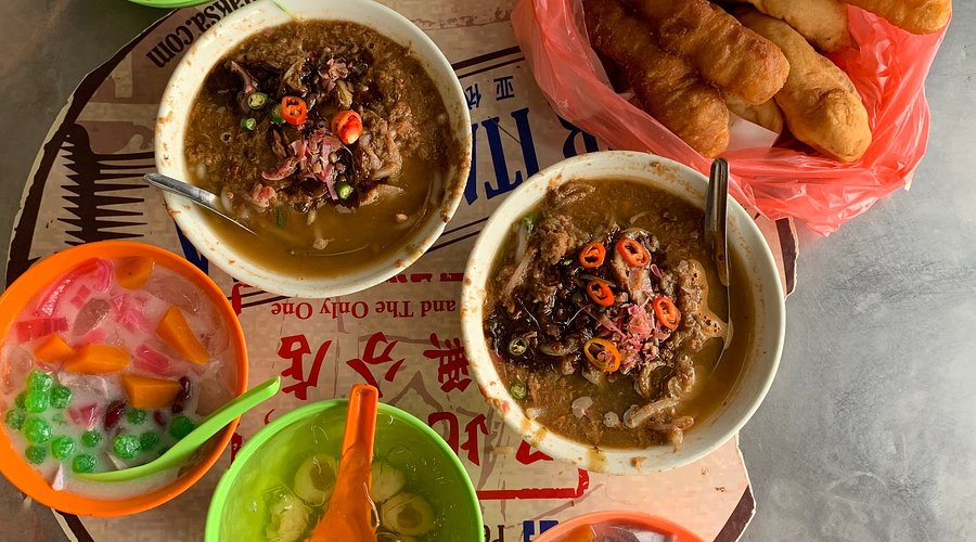 A bowl of Assam Laksa, showcasing the thick rice noodles, the rich broth, and the various toppings, including shredded cucumber, onions, and mint.