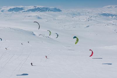 A lone kite sledder silhouetted against the vast, snow-covered Hardangervidda Plateau under a winter sky.