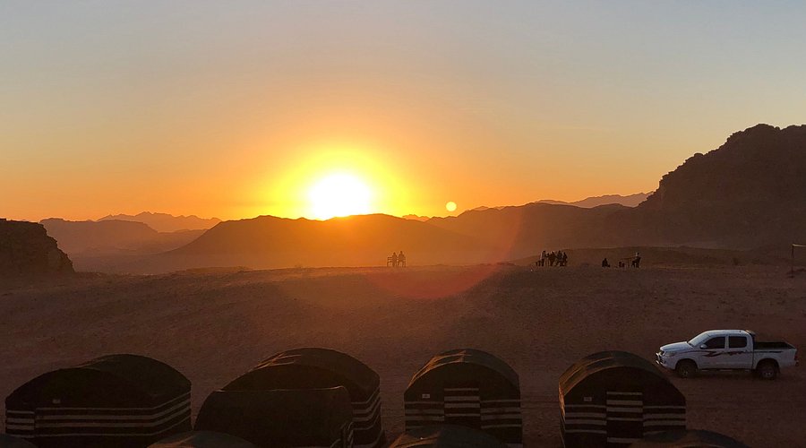 Panoramic view of Wadi Rum, Jordan, showcasing the vast desert landscape with towering sandstone mountains and a clear blue sky.