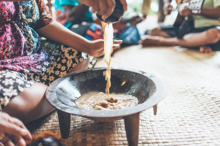A group of tourists participating in a Kava ceremony in a Fijian village, highlighting the cultural experiences available in the Yasawa Islands.