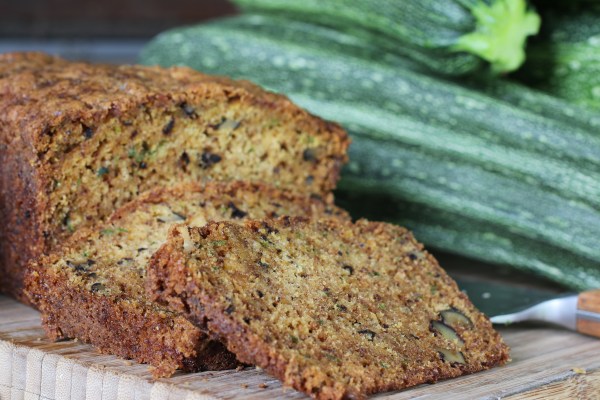 A slice of zucchini bread with honey-lavender glaze on a plate, with a cup of tea or coffee in the background.