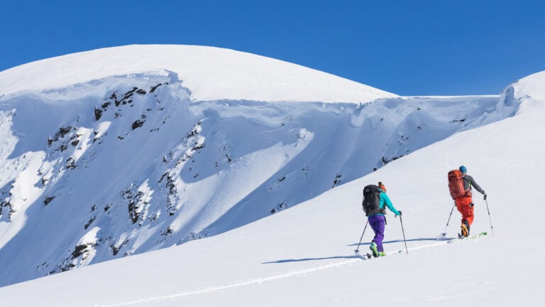 A helicopter landing on a snow-covered mountain peak in the Purcell Mountains, with snowshoers preparing to disembark. The image demonstrates the heli-snowshoeing experience offered by White Mountain Adventures, emphasizing the remote and pristine wilderness.