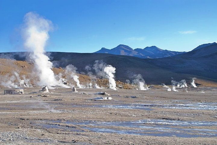 The geothermal field of El Tatio geysers in the Atacama Desert, Chile, with steam rising from the geysers against a backdrop of rugged mountains.