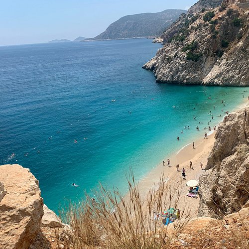A serene view of Antisamos Beach in Kefalonia, Greece, capturing the crystal-clear turquoise water, white pebble beach, and lush green hills.