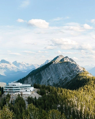 View from atop a mountain overlooking a vast landscape of mountain ranges and forests. The image captures the sense of being above the world and the breathtaking panoramic views from the Banff Gondola.