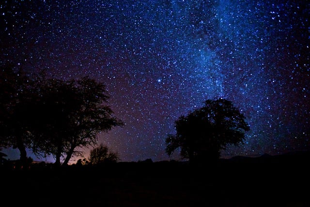 Wide-angle shot of the Atacama Desert at night, capturing the Milky Way stretching over the Valle de la Luna, with a solitary ALMA telescope visible in the distance.