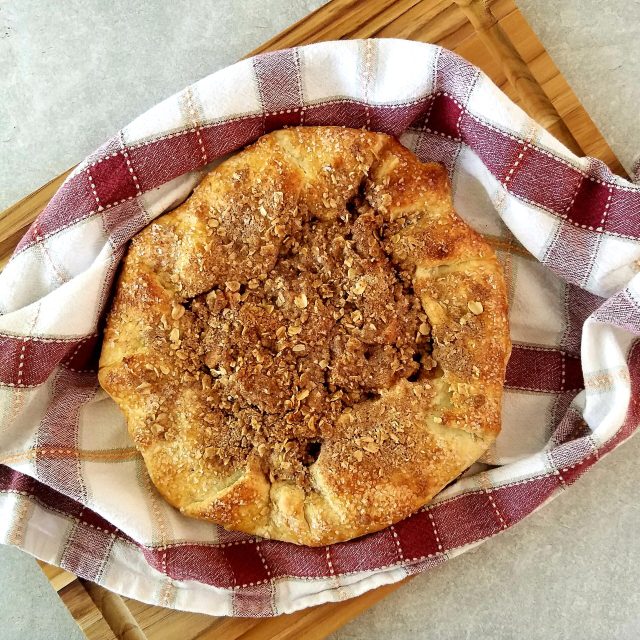 An eye-level photograph of the apple crumble baking in the oven, with the oven light illuminating the bubbling apple filling and golden-brown oat topping.