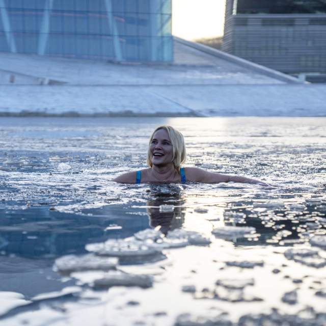 A person emerging from an icy fjord, surrounded by snow-covered mountains. This image captures the invigorating experience of ice bathing in the Arctic.