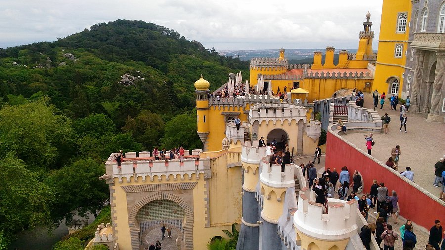 descriptive alt text: A panoramic view of Pena Palace perched atop the Serra de Sintra mountains, showcasing its vibrant colors and stunning architecture. This illustrates the overall beauty and visual appeal of Sintra