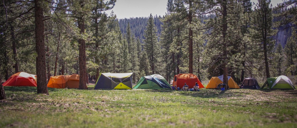 The Chen family poses in front of their tent in Yosemite, looking happy but slightly disheveled. The tent is in the background, and the warm, natural lighting captures the golden hour glow.
