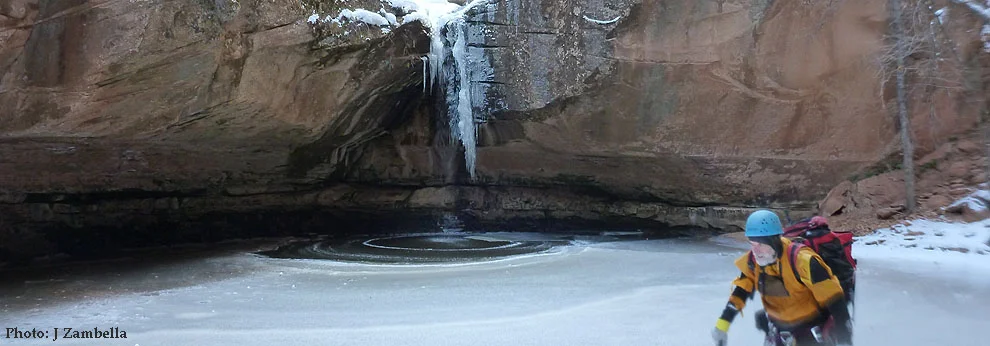 Canyoneers descend a narrow canyon in Zion National Park, showcasing the contrast of red rock, snow, and ice.