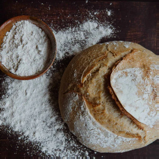 A family gathered around a candlelit table, sharing a meal of soup in sourdough bread bowls, enjoying the warmth and togetherness of the Winter Solstice.