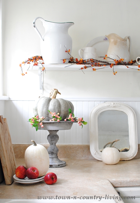 A farmhouse kitchen island adorned with a variety of pumpkins, gourds, and candles.