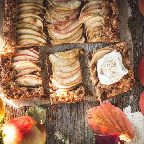 A crate of freshly harvested heirloom apples, including Roxbury Russet, Northern Spy, and Calville Blanc d'Hiver. The apples are displayed in a rustic wooden crate with autumn leaves scattered around them, highlighting their natural beauty.