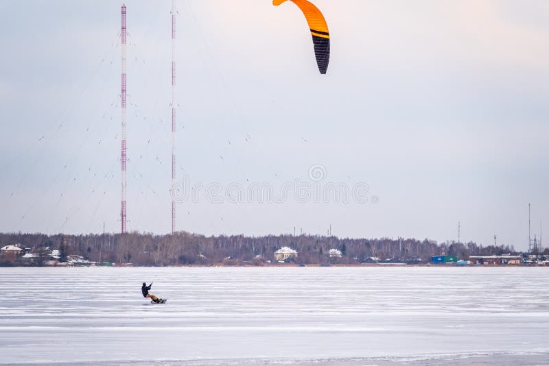 Wide shot of a snowkiter soaring high above the icy expanse of Lake Michigan, silhouetted against a winter sunset