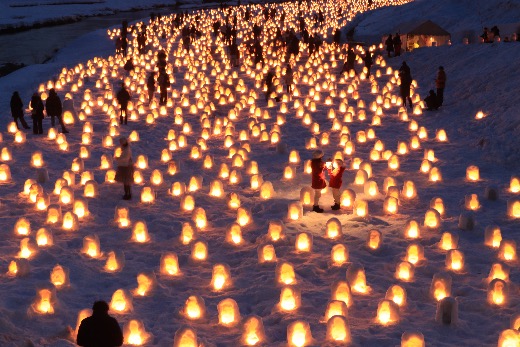 A group of people ice fishing on Lake Shikaribetsu, with tents and snow-covered mountains in the background.