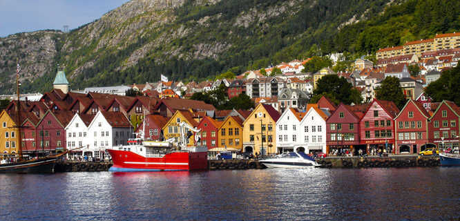 A hand reaches for a heart-shaped Vaffel in Bryggen, Bergen. The golden hour light and colorful buildings create a warm and inviting scene, highlighting the delicious treats and charming atmosphere that Bergen has to offer for solo travelers.