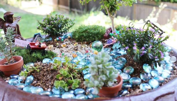 A collection of fairy garden supplies laid out on a table, including a terracotta pot, various succulents, pebbles, twigs, and miniature figurines.