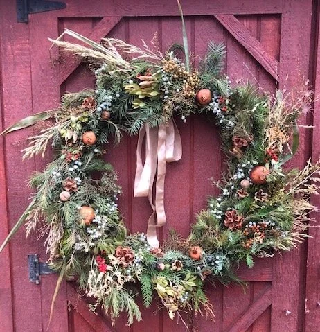 A person organizing the foraged materials, separating different types of greenery, berries, and pinecones into piles.