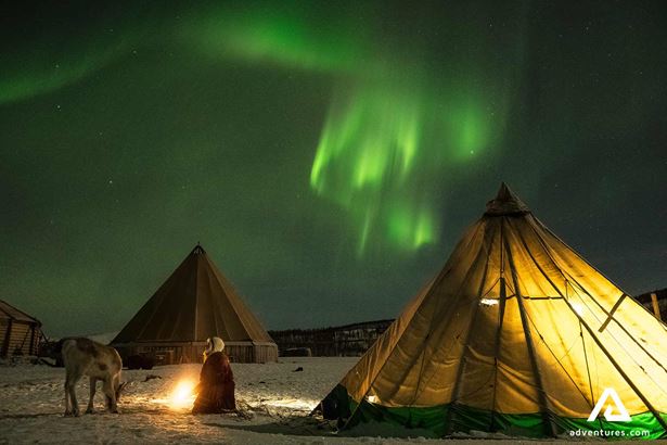 The warm glow of a fire inside a Sami Lavvu, with the Northern Lights dancing in the sky above. The image conveys a sense of warmth, community, and the magic of the Arctic night.