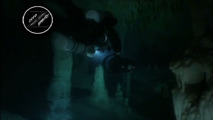 Divers navigating narrow passages in a Yucatan cenote, illuminated by their dive lights.