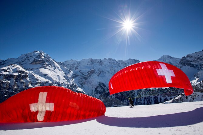 A wide-angle shot from the perspective of a paraglider, showing the snow-capped mountains, turquoise lakes, and the town of Interlaken below. This emphasizes the stunning panoramic views available from paragliding.