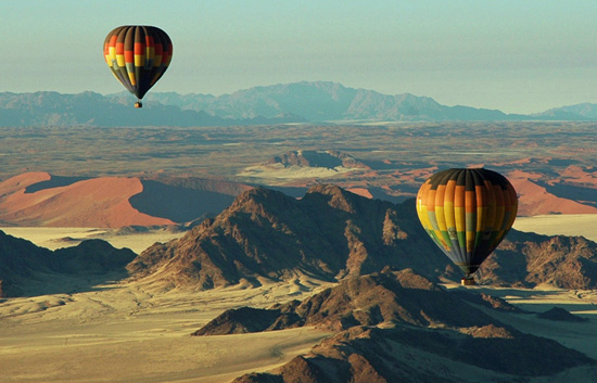 Hot air balloon view of Sossusvlei at sunrise, showcasing the interplay of light and shadow on the towering red dunes