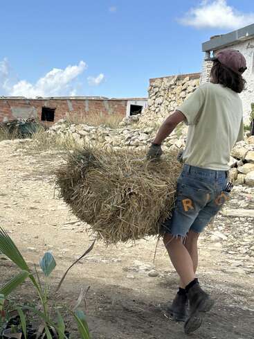 Two people on a farm are using shovels to work with a pile of compost, demonstrating the composting process.