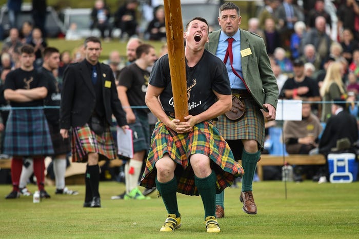 A competitor mid-toss at the Braemar Highland Games, with the rugged Highland landscape as the backdrop