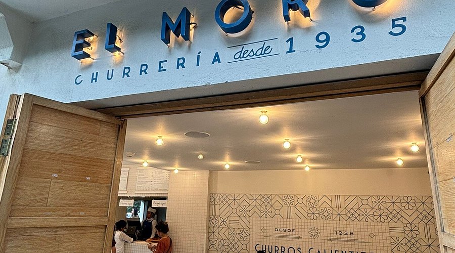 A vertical spit of al pastor meat being cooked, with a vendor shaving off slices.