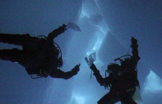 A steaming bowl of traditional Norwegian fish soup with chunks of salmon and vegetables, garnished with fresh herbs, sitting on a rustic wooden table at Fjordcamp.