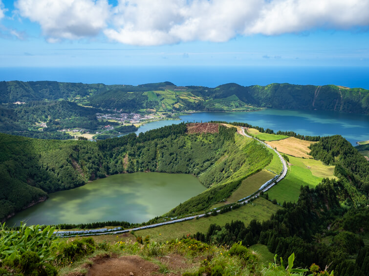 Panoramic view of the Sete Cidades caldera with twin lakes, vibrant greenery, and changing weather conditions.