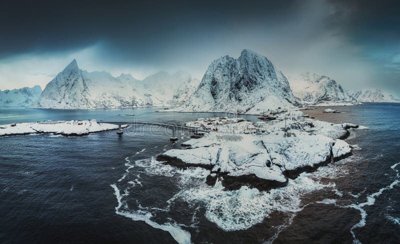 A surfer silhouetted against the backdrop of snow-covered mountains and the Northern Lights reflected in the water.