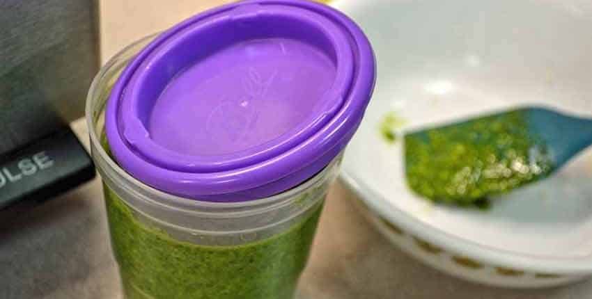 Close-up shot of fresh herbs, like basil, packed into an ice cube tray and covered in olive oil, ready to be frozen.