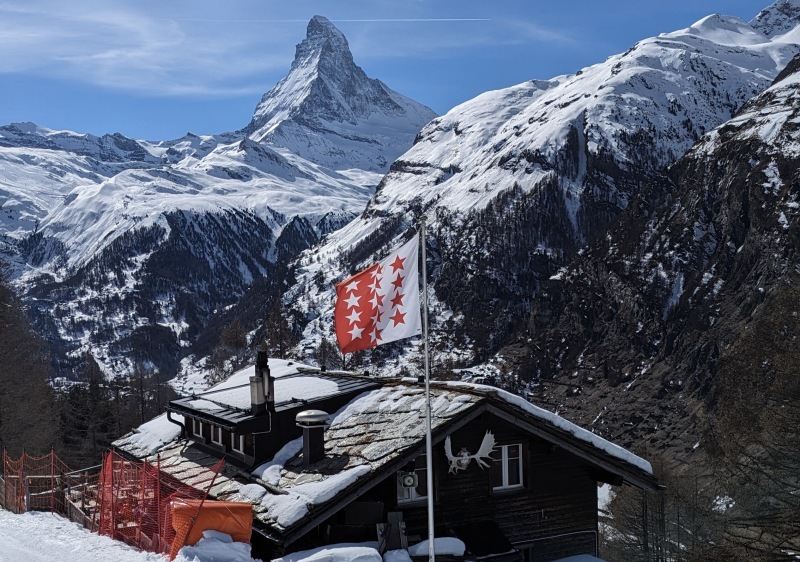 A couple silhouetted against the Matterhorn at sunset, champagne flutes in hand, wearing luxury ski gear.