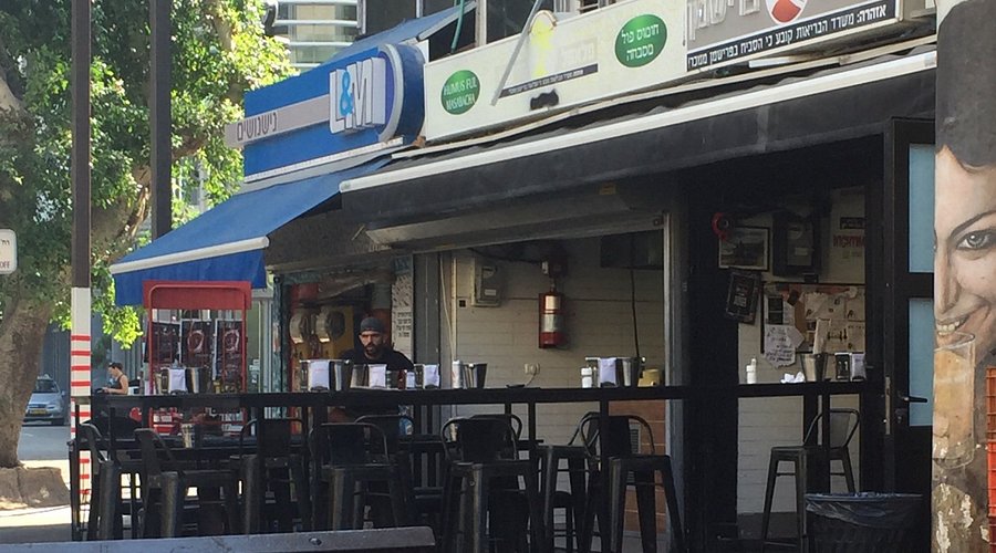 A perfectly assembled Sabich sandwich from Sabich Frishman, showcasing layers of fried eggplant, hard-boiled egg, hummus, tahini, Israeli salad, amba, and parsley, all nestled in a fluffy pita bread, representing the explosion of flavors and textures