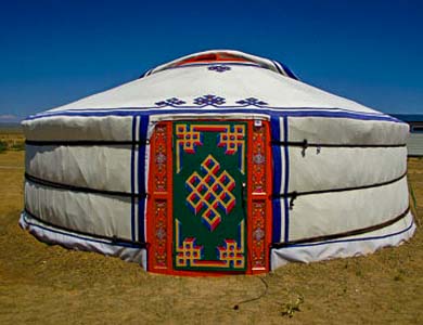 A Mongolian nomad teaching a tourist how to construct a Ger, with camels grazing in the background