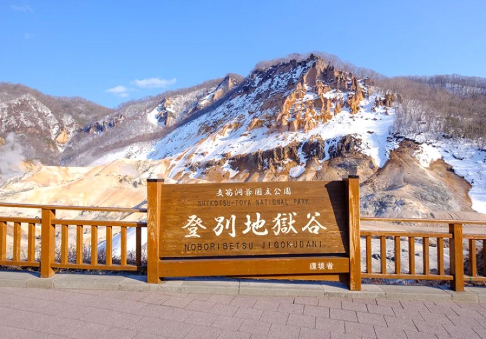 A snowmobile traversing a snow-covered slope with a smoking volcanic crater in the background. Motion blur conveys speed; emphasizing the contrast between the white snow and the dark volcanic rock