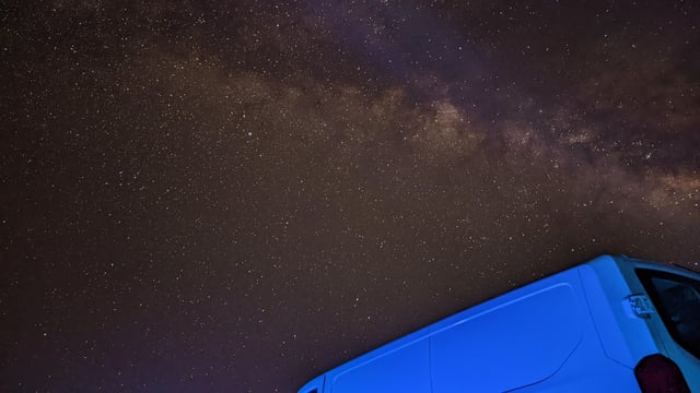 A beautiful night sky filled with stars is captured above a landscape with trees and a distant hill, creating a stunning celestial view.