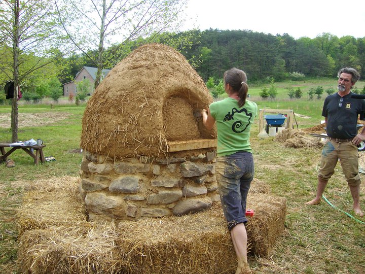 Partially constructed cob oven showing brickwork, clay, and straw.