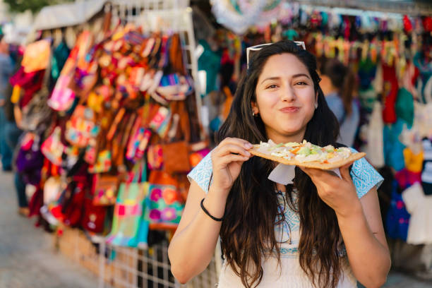 Tlayuda photo: Overhead shot of a Tlayuda at a market stall, highlighting the variety of toppings and the crispy texture of the tortilla. The background should show the bustling market scene, adding context and vibrancy. Use natural, slightly diffused lighting.