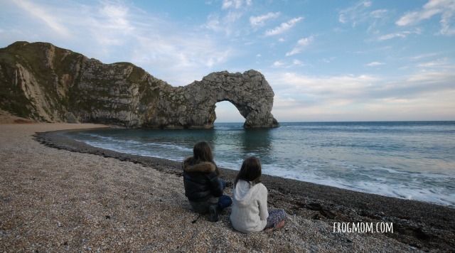A family enjoying the sunset celebration at Pier 60 in Clearwater Beach. The children are laughing and pointing at street performers, while the parents watch with smiles, all set against a backdrop of a colorful sunset sky.